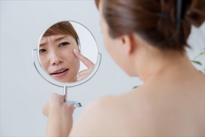 鏡で顔のできものをチェックする女性